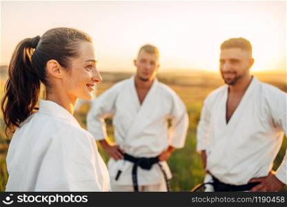 Two male and one female karate fighters on training in summer field. Martial art workout outdoor, technique practice