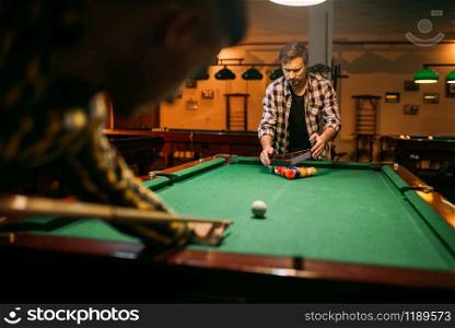 Two male billiard players with cue at the table with colorful balls. Men plays american pool in sport bar. Two male billiard players with cue at the table