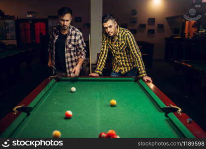 Two male billiard players with cue at the table with colorful balls, poolroom. Men plays american pool game in sport bar. Two male billiard players with cue, poolroom