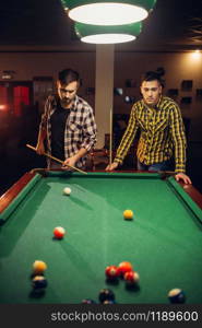 Two male billiard players with cue at the table with colorful balls, poolroom. Men plays american pool game in sport bar