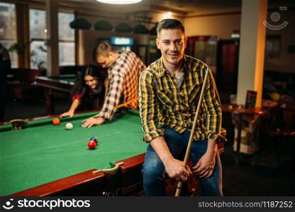Two male billiard players with cues poses at the table with colorful balls, poolroom. Men plays american pool game in the sport bar. Two male billiard players with cues poses