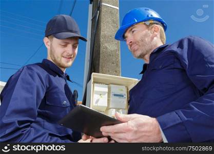 two male electricians with clipboard by outdoor meter