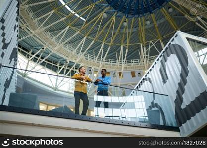 Two male employees are talking on the balcony in IT office. Professional teamwork and planning, group brainstorming, modern company interior on background. Two employees talking on the balcony in IT office