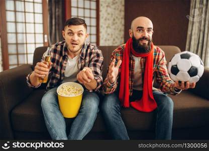 Two male football fans wathing tv broadcast at home. Friends with beer and popcorn cheer for their favorite team. Two football fans wathing tv broadcast at home