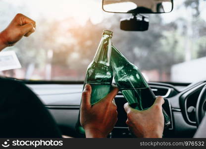 Two male friends are celebrating in the car while they are clinking beer bottle together.