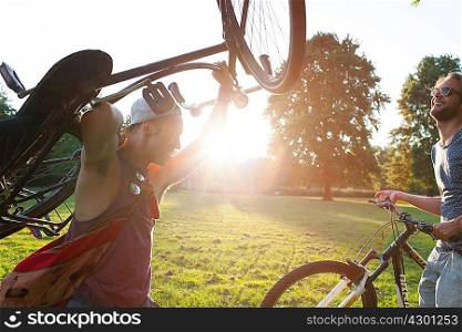 Two male friends arriving in park with bicycles at sunset