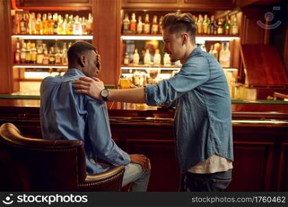 Two male friends drinks beer at the counter in bar. People relax in pub, night lifestyle, friendship, event celebration. Male friends drinks beer at the counter in bar