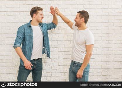two male friends giving high five each other against white brick wall
