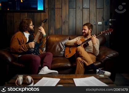 Two male friends playing guitar at home together. Musicians enjoy hobby activity at home studio. Male friends playing guitar at home together