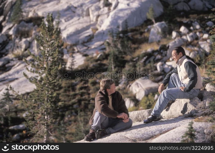 Two Male Friends Sitting On A Rock In The Mountains And Enjoying Each Other&acute;s Company