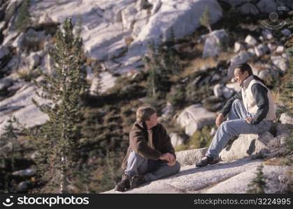 Two Male Friends Sitting On A Rock In The Mountains And Enjoying Each Other&acute;s Company
