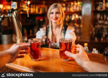 Two male friends takes beer from waitress at the counter in pub. Men with mugs having fun in bar, barmaid in traditional retro style. Two friends takes beer from waitress, oktoberfest