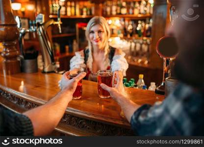Two male friends takes beer from waitress at the counter in pub. Men with mugs having fun in bar, barmaid in traditional retro style