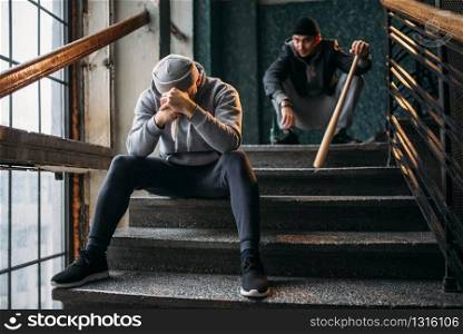 Two male gangsters are sitting on the stairs. Street robbers with baseball bat and knife waiting for victim. Crime concept