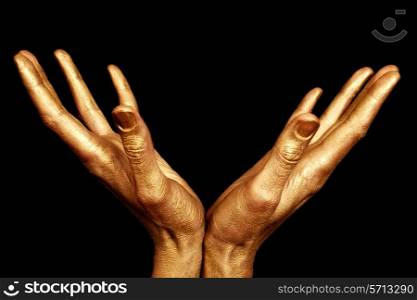 Two male hands in gold paint isolated on a black background