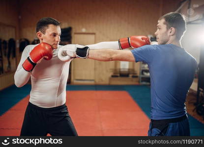 Two male kickboxers in gloves practicing on workout in the gym. Fighters on training, kickboxing practice in action, sparring partners. Two male kickboxers practicing on workout in gym