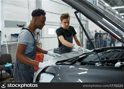 Two male mechanics checking motor, car service. Vehicle repairing garage, men in uniform, automobile station interior on background. Professional auto diagnostic. Two male mechanics checking motor, car service
