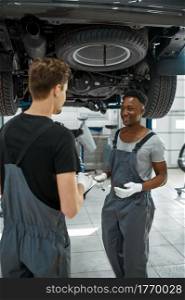 Two male mechanics looking on checklist, car service. Vehicle repairing garage, men in uniform, automobile station interior on background. Professional auto diagnostic. Male mechanics looking on checklist, car service