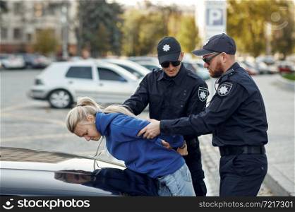 Two male police officers arrest female driver. Policemen in uniform protect the law, registration of an offense. Cops work on city street, order and justice control. Two male police officers arrest female driver