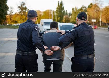 Two male police officers arrest young man. Policemen in uniform protect the law, registration of an offense. Cops work on city street, order and justice control. Two male police officers arrest young man