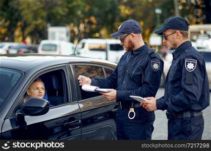 Two male police officers checking the driving license. Policemen in uniform protect the law, registration of an offense. Cops work on city street, order and justice control. Male police officers checking the driving license
