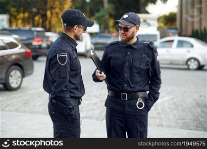 Two male police officers in sunglasses. Policemen in uniform protect the law, registration of an offense. Cops work on city street, order and justice control. Two male police officers in sunglasses