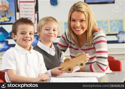 Two Male Primary School Pupils And Teacher Working At Desk In Classroom