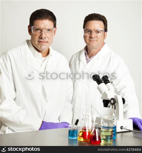 Two male scientists in their laboratory, with microscope and beakers of chemicals.