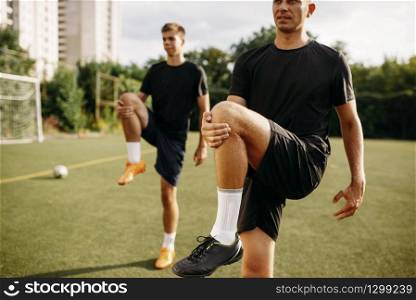 Two male soccer players doing stretching exercise on the field. Football training on outdoor stadium, workout before game. Male soccer players doing stretching exercise