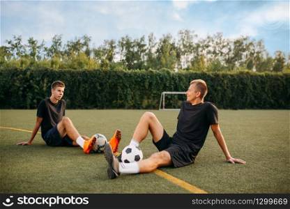 Two male soccer players resting on the grass on the field. Footballers on outdoor stadium, workout before game, football training. Two male soccer players resting on the grass