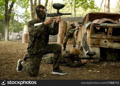 Two male warriors in camouflages and masks aimimg with paintball guns. Extreme sport with pneumatic weapon and paint bullets or markers, military team game outdoors, combat tactics. Two male warriors aimimg with paintball guns