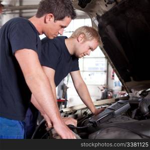 Two man mechanics looking a diagnostics equipment, servicing car