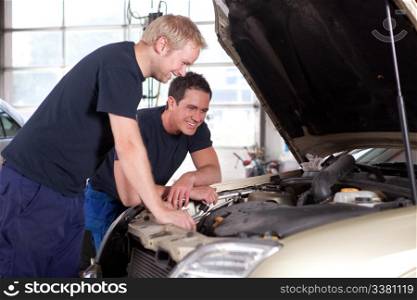 Two man mechanics smiling and working under the hood of a car, shallow depth of field, sharp focus on rear mechanic