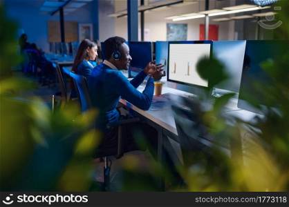 Two managers works in night office, back view. Male and female workers, dark business center interior on background, modern workplace. Two managers works in night office, back view
