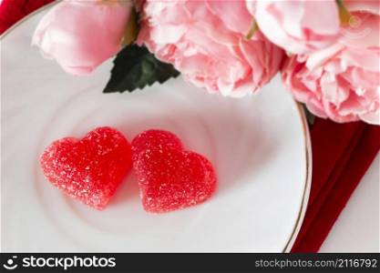 Two marmalade hearts on a white saucer. Symbol of love and valentines day. Two marmalade hearts and flowers