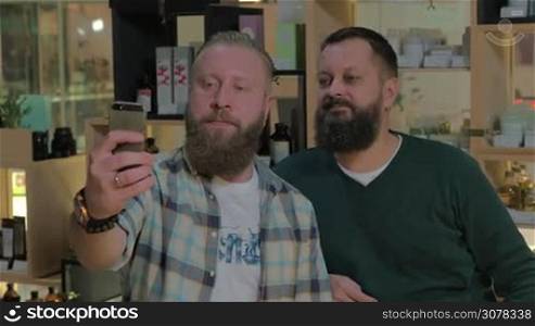 Two mature bearded men taking cellphone selfie in the barbershop