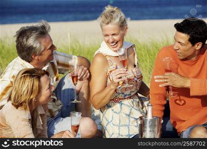 Two mature couples sitting on the beach and holding champagne flutes