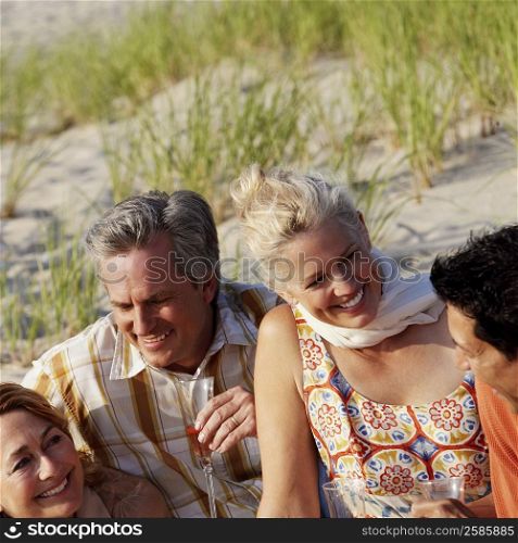 Two mature couples sitting on the beach and smiling