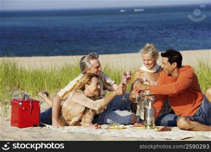 Two mature couples sitting on the beach and toasting with champagne