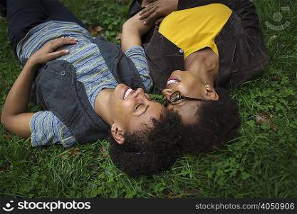 Two mature female friends lying on park grass