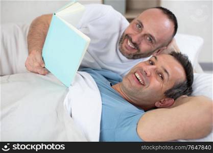 two mature men in bed looking at a book