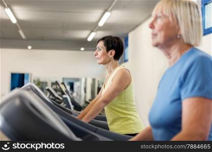 Two mature women are running on a treadmill in the fitness studio