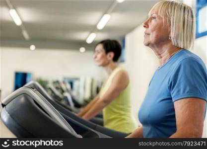 Two mature women are running on a treadmill in the fitness studio
