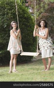 Two mature women holding a rope swing and smiling