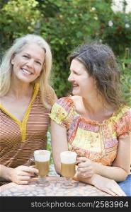 Two mature women holding cold coffee cups and smiling