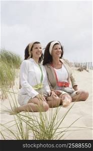 Two mature women kneeling on the beach and smiling