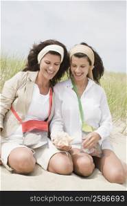Two mature women looking at a conch shell on the beach and smiling