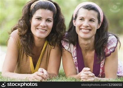 Two mature women lying on grass and smiling