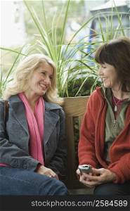 Two mature women sitting on a bench and talking to each other