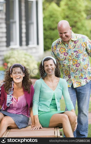 Two mature women sitting on a lounge chair with a mature man standing beside them